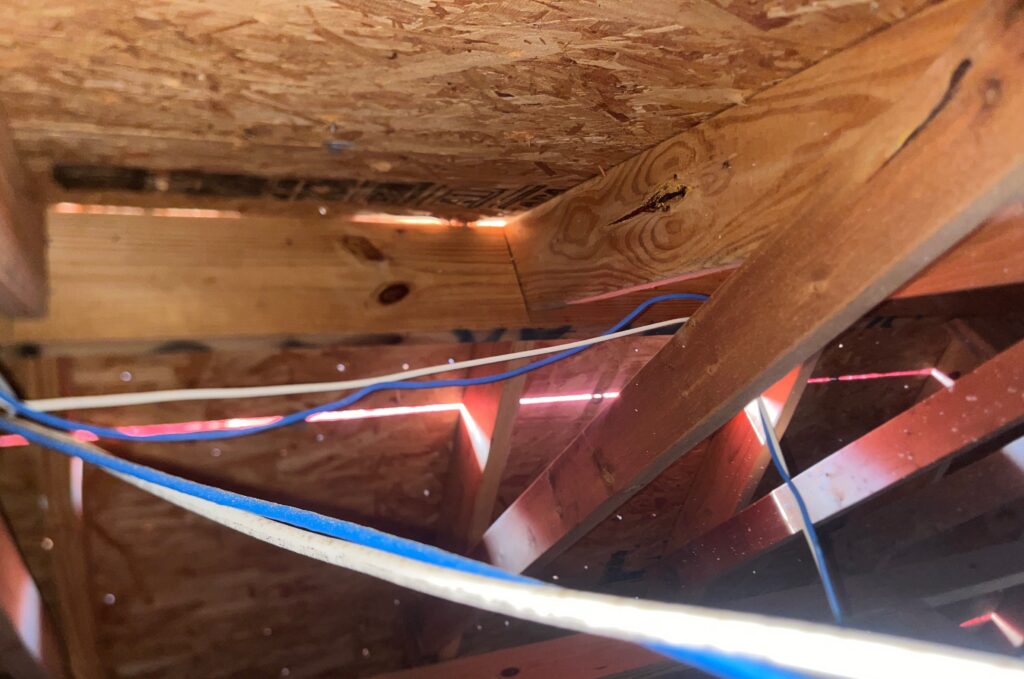 This image shows gaps in the attic roof deck and soffit area, which allow daylight to penetrate into the roof structure. These openings likely indicate improper ventilation or poorly sealed roof decking.