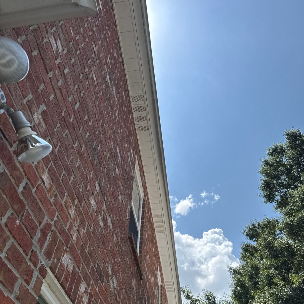 An upward-facing exterior view of a brick wall and white soffit area. The image captures the siding and roofline junction during an inspection.
