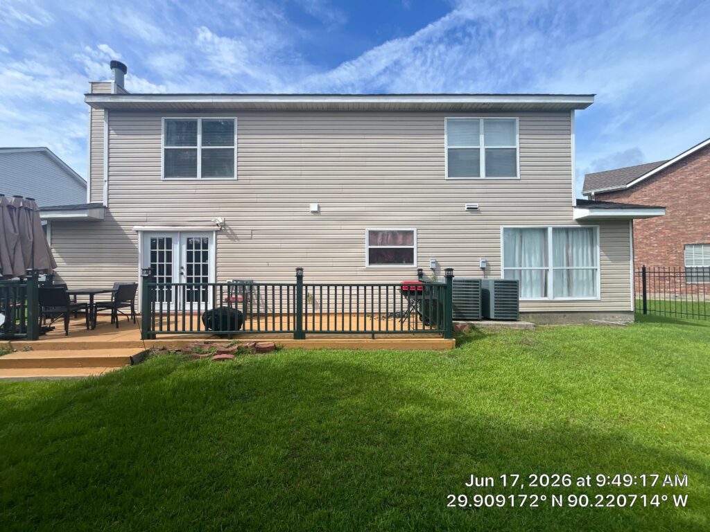 This is a straight-on exterior view of the back of a two-story residential home with beige vinyl siding. The photo shows a wooden deck, a set of French doors, various windows, and two air conditioning units positioned near the back wall.
