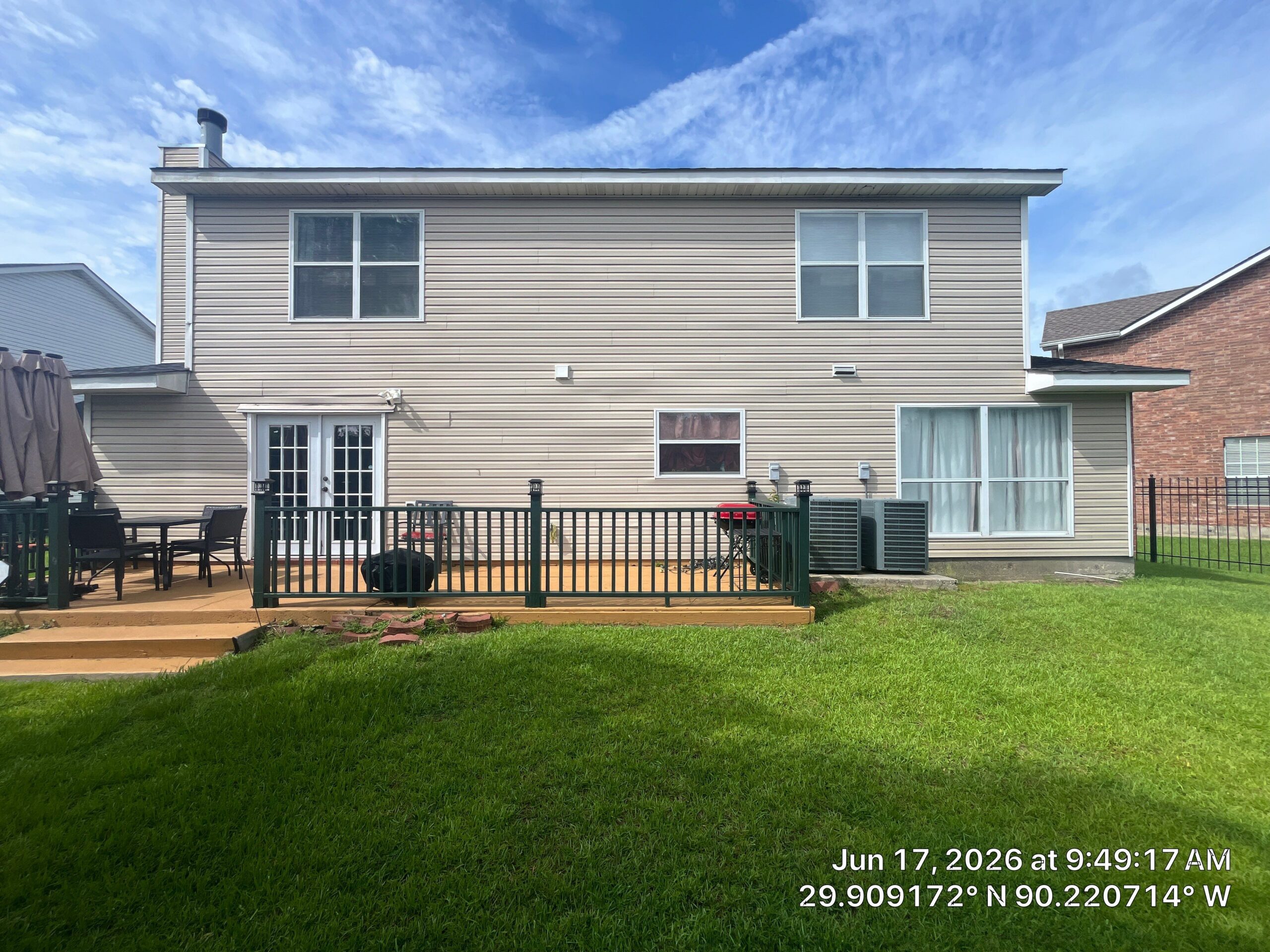 This is a straight-on exterior view of the back of a two-story residential home with beige vinyl siding. The photo shows a wooden deck, a set of French doors, various windows, and two air conditioning units positioned near the back wall.