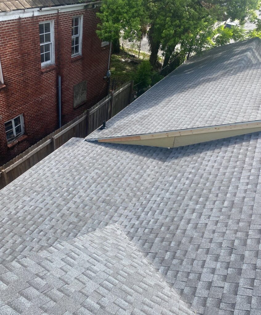 An aerial view of an asphalt shingle roof showing a recent repair area where new fascia board and drip edge flashing have been installed along the edge of a roof section.