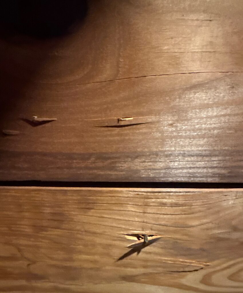 This photo shows exterior wood fascia or trim boards with visible splitting and nail pops. The wood appears to be weathering, and the fasteners have caused the material to crack.
