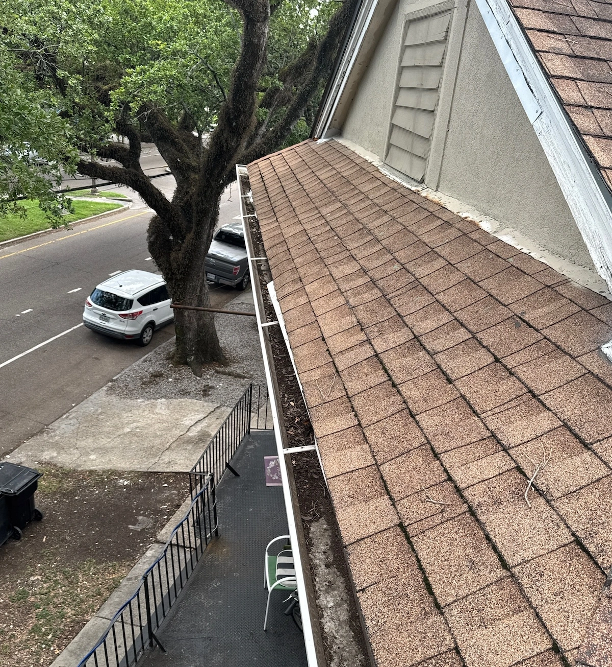 Overhead view of an asphalt shingle roof and adjacent gutter filled with debris